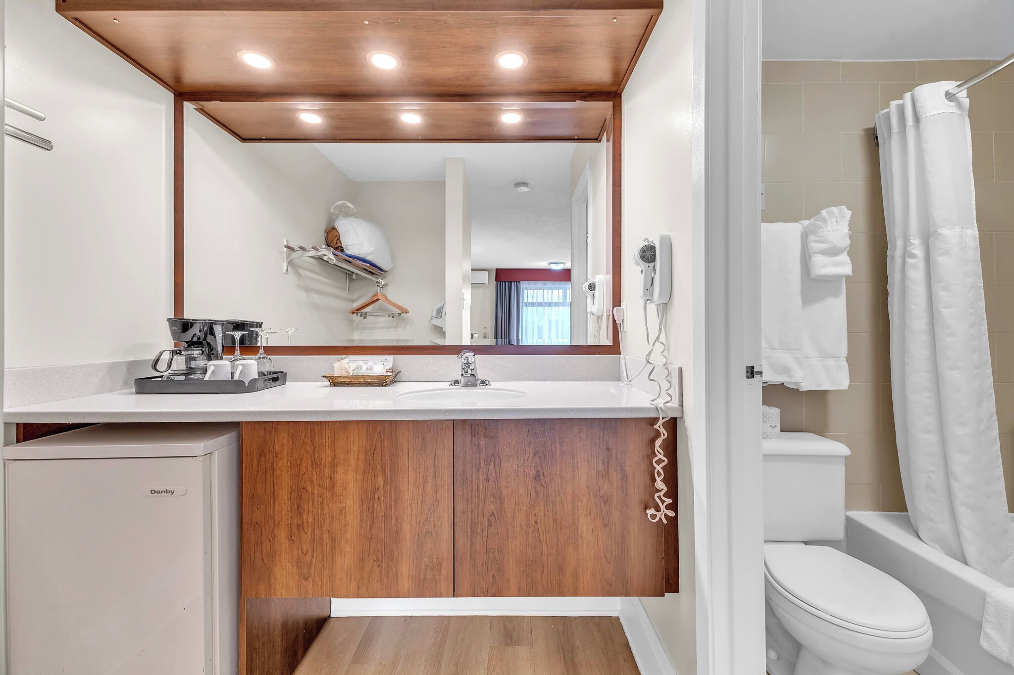 A modern bathroom with a wooden vanity, a Danby refrigerator, a shower curtain, and a toilet.