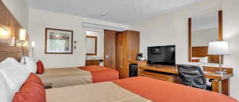 Una habitación de hotel con dos camas, un escritorio, un televisor y un espejo.