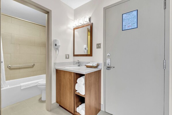 Une salle de bain équipée d’une baignoire, d’un lavabo, d’un miroir et d’une porte sur laquelle est apposé un panneau bleu indiquant la sortie de secours.