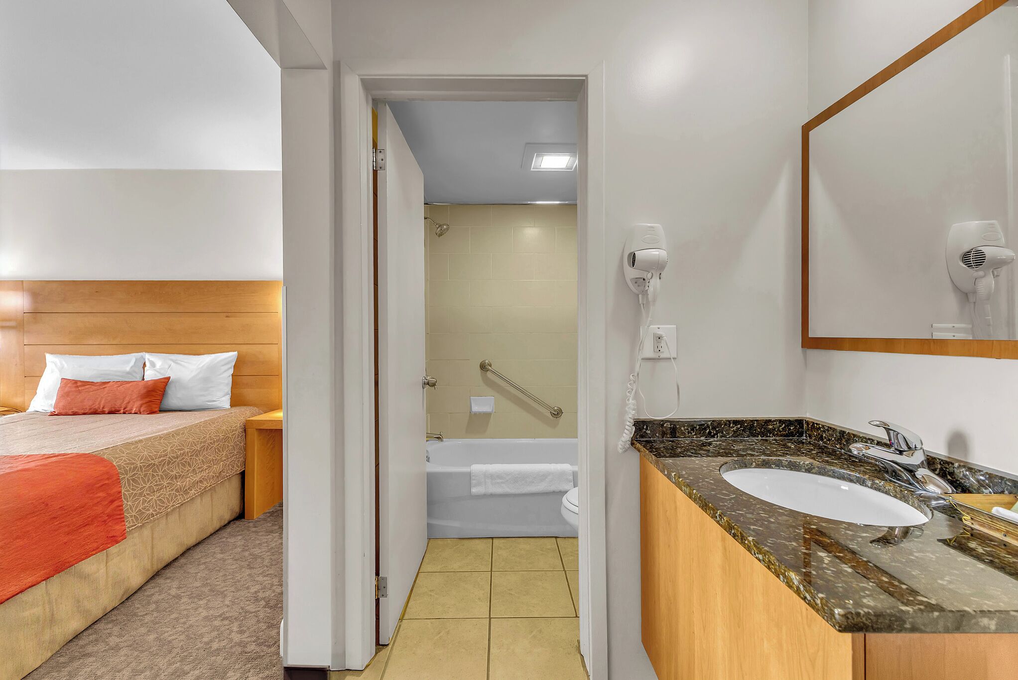 Una habitación de hotel con cama, baño con bañera, lavamanos y secador de pelo.