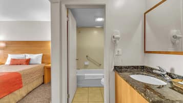 Una habitación de hotel con cama, baño con bañera, lavamanos y secador de pelo.