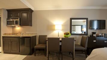 Habitación de hotel con kitchenette, comedor con sillas y mesa, lámpara, espejo y televisor.
