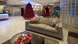A modern lobby with a large Christmas tree, a reception desk, and a seating area with a sofa and armchairs. - Visitors Inn (Hamilton)