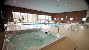 An indoor swimming pool with a hot tub, lounge chairs, and a brick wall with windows. - Visitors Inn (Hamilton)