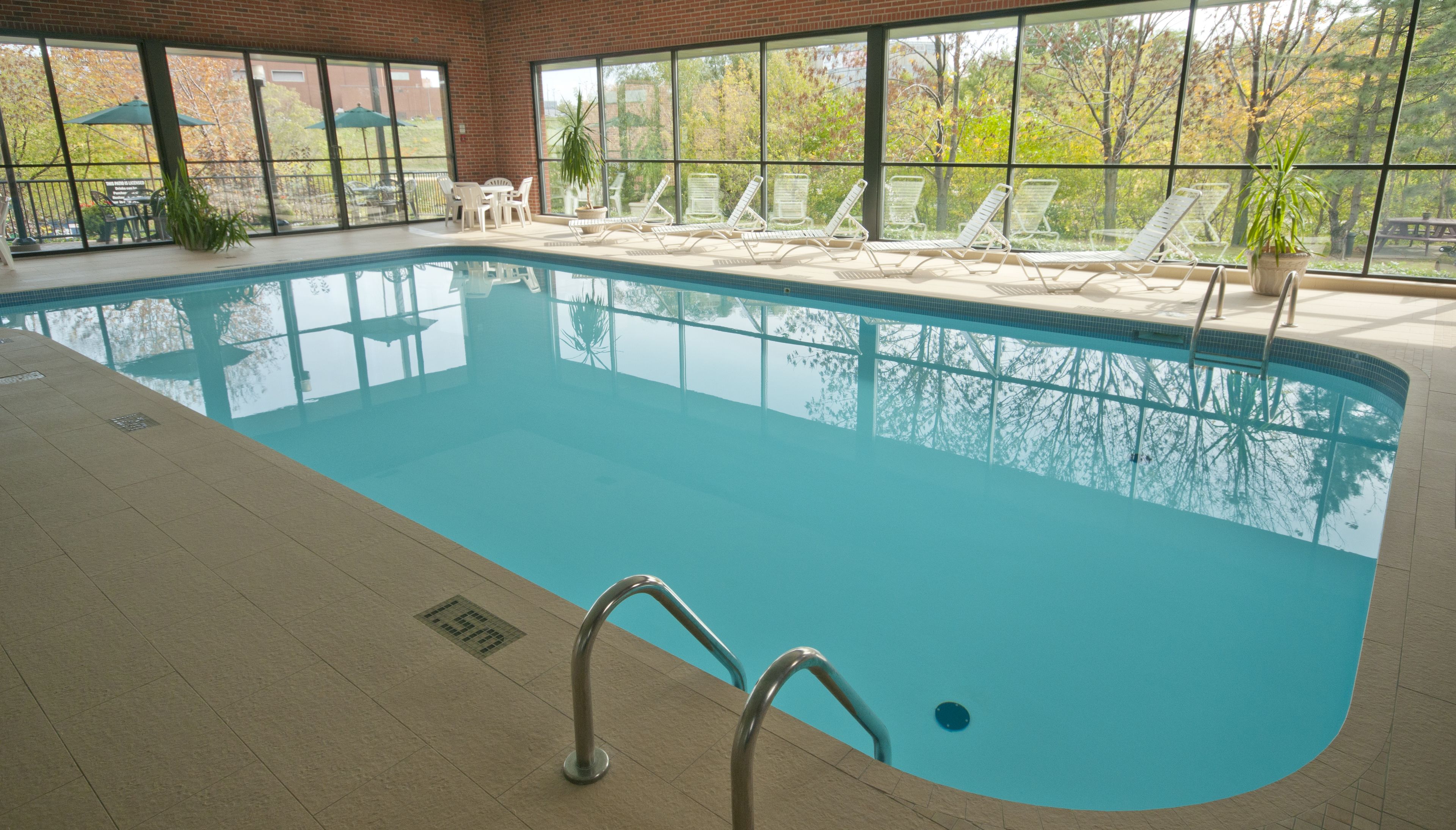 An indoor swimming pool with clear glass walls, a tiled floor, and several lounge chairs around the perimeter.