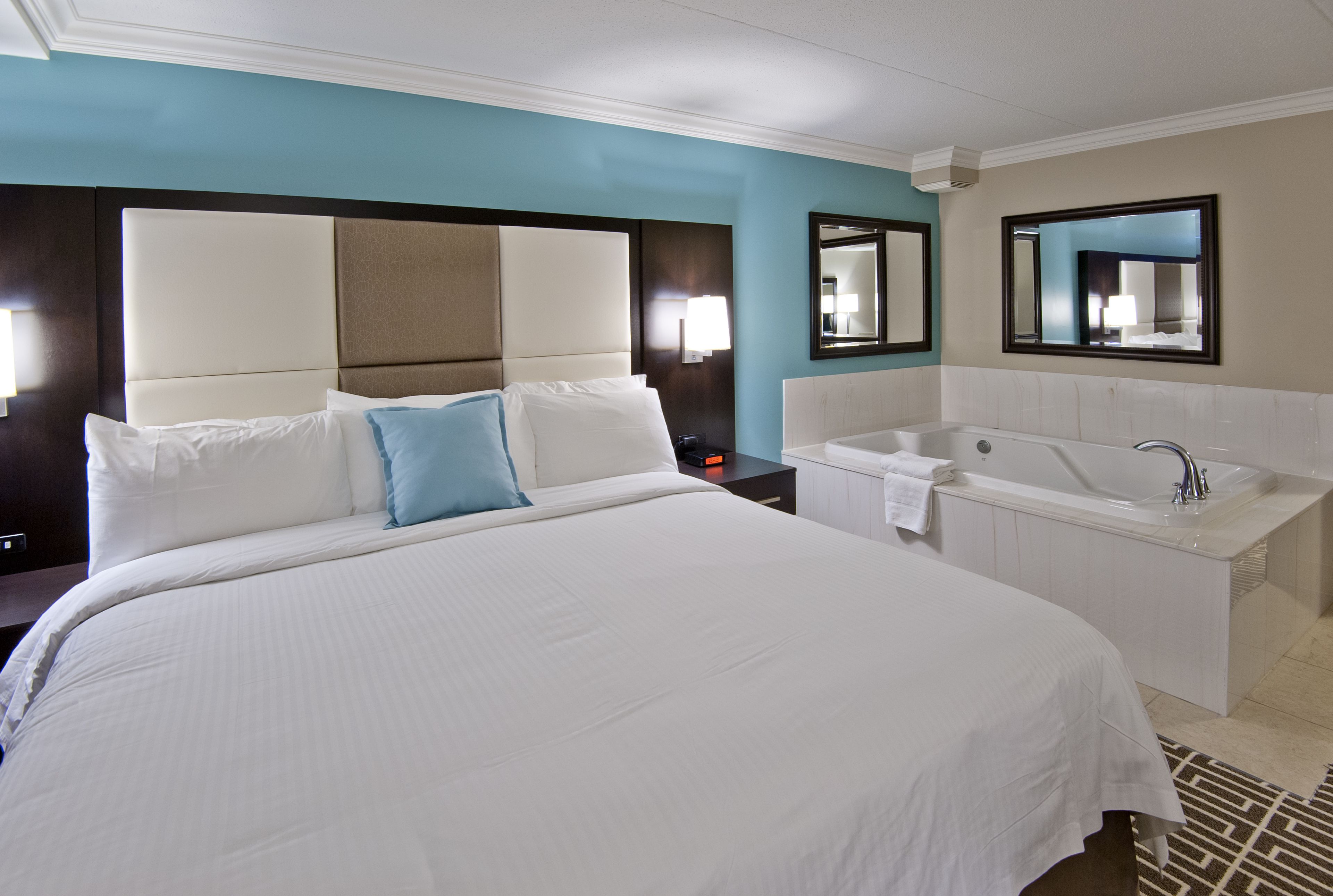 Quarto de hotel com uma cama grande, banheiro separado com banheira e duas espelhos fixados na parede.
