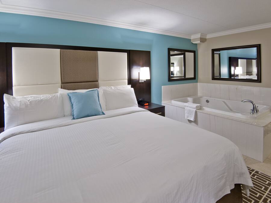 A hotel room with a large bed, a separate bathroom with a bathtub, and two wall-mounted mirrors.