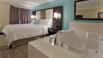 A hotel room with a large bed, a separate sitting area, a bathtub, and a large mirror.