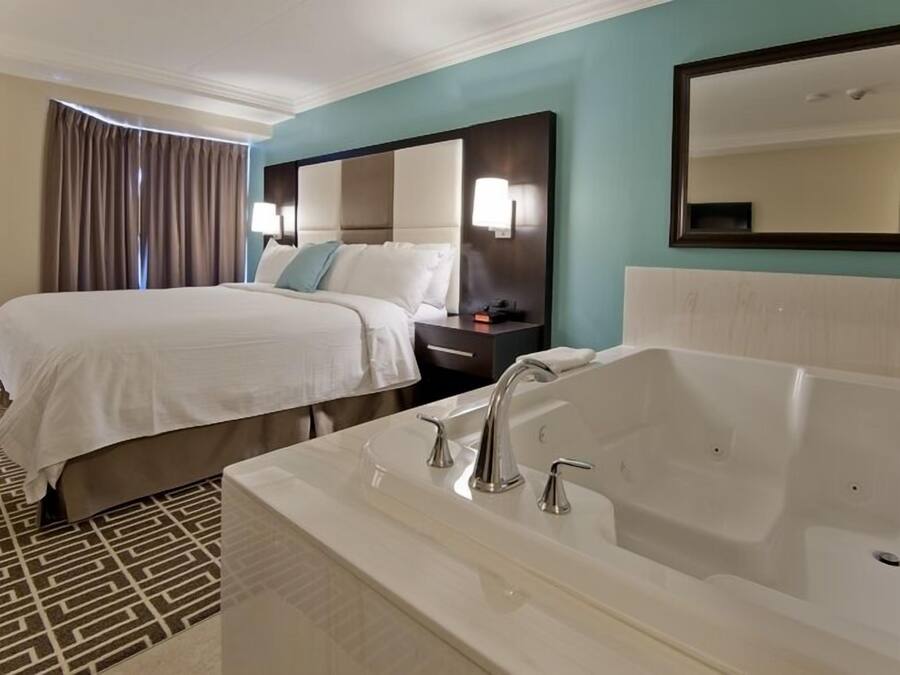 A hotel room with a large bed, a separate sitting area, a bathtub, and a large mirror.