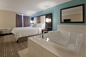 A hotel room with a large bed, a separate bathroom with a bathtub, and a large mirror on the wall.