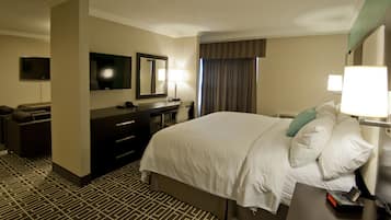 Une chambre d’hôtel avec un grand lit, un bureau avec une chaise, un téléviseur à écran plat, un miroir, une lampe et une moquette à motifs.