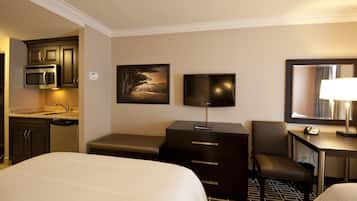 Habitación de hotel con cama, escritorio con lámpara, televisor, silla, mesita pequeña, microondas y lavamanos.