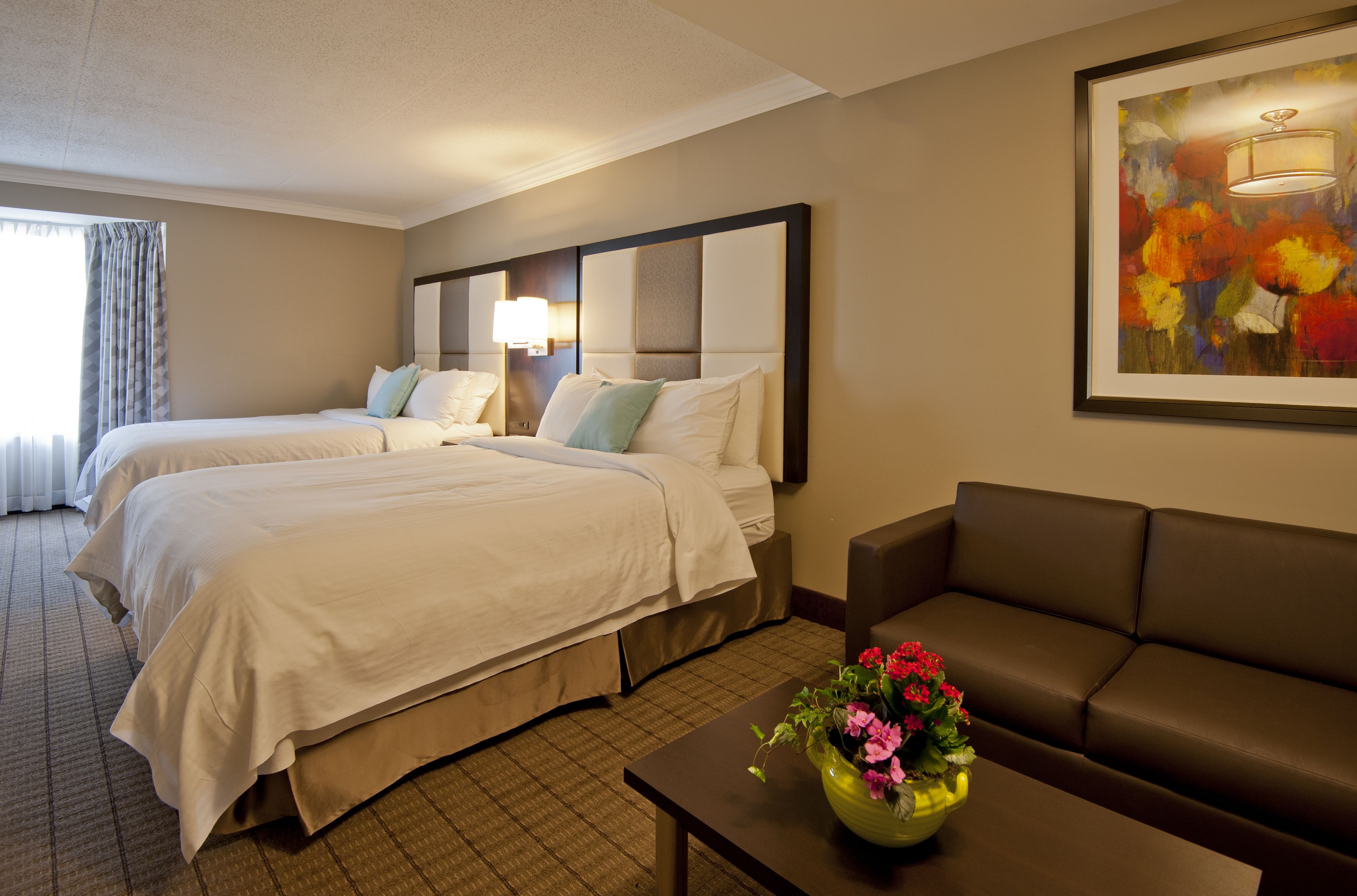 A hotel room with two beds, a sofa, a coffee table, and a painting on the wall.