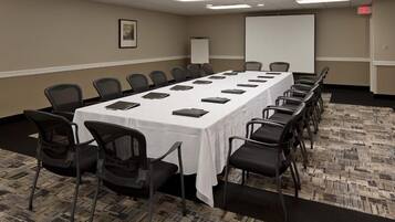 A conference room with a long table, chairs, a projector screen, and a whiteboard.