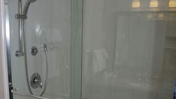 Una ducha con cerramiento de vidrio, cabezal de ducha de mano y grifo empotrado.