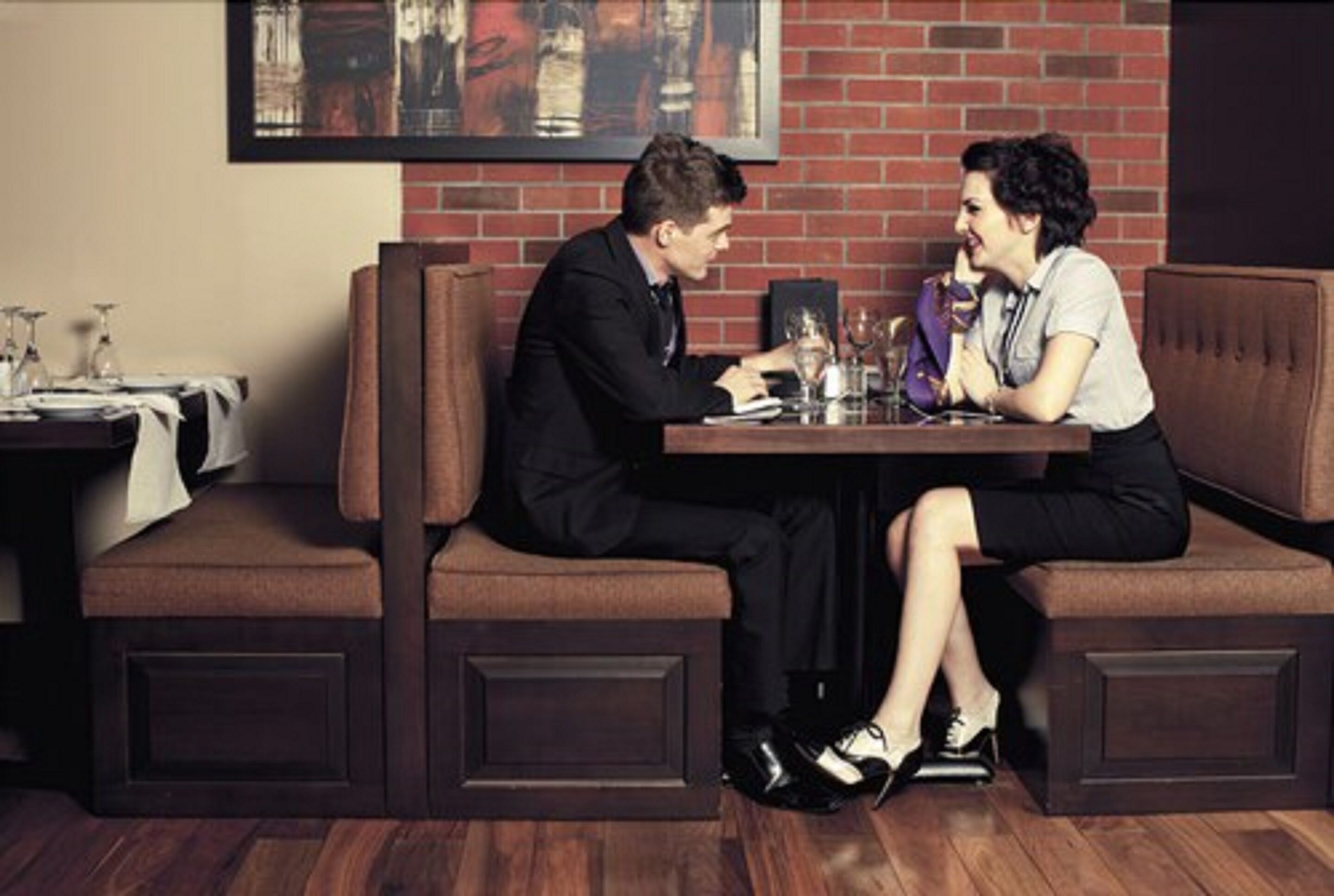 Un homme et une femme sont assis à une table dans un restaurant, avec un mur de briques en arrière-plan.