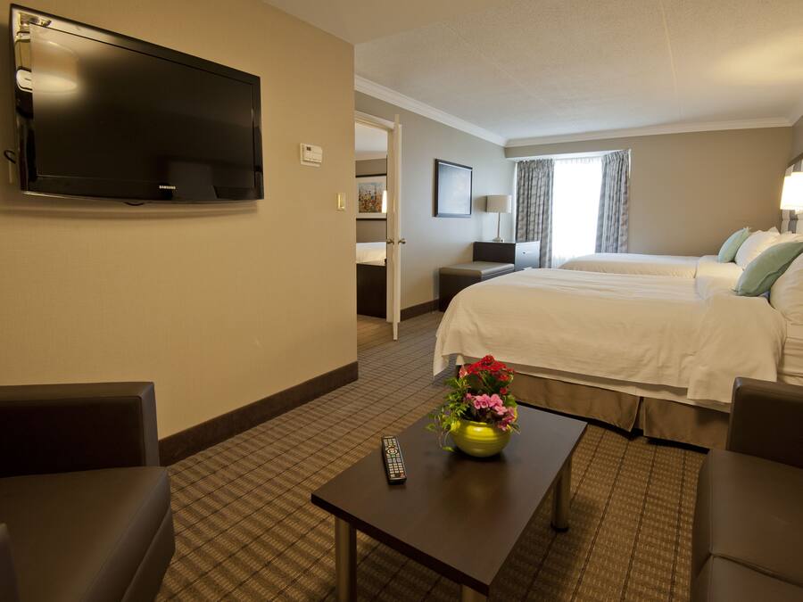 A hotel room with a flat-screen TV mounted on the wall, a bed with white linens, a small table with a vase of flowers, and a remote control on the table.