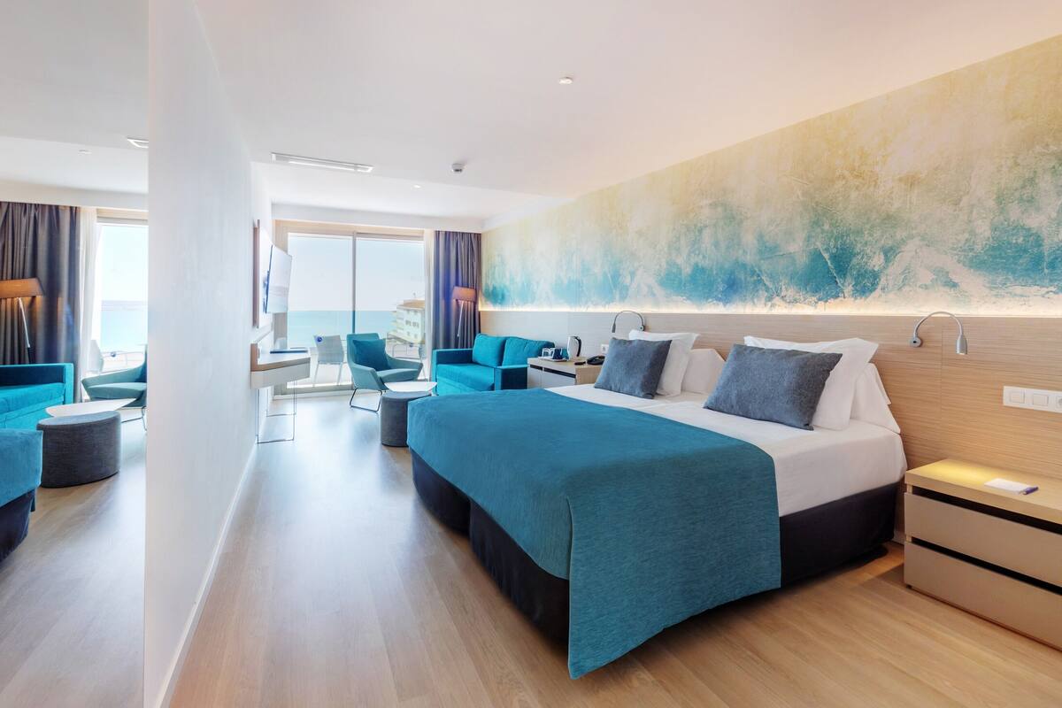 Habitación de hotel moderna con una cama grande, un escritorio y un área de descanso con vista al mar.