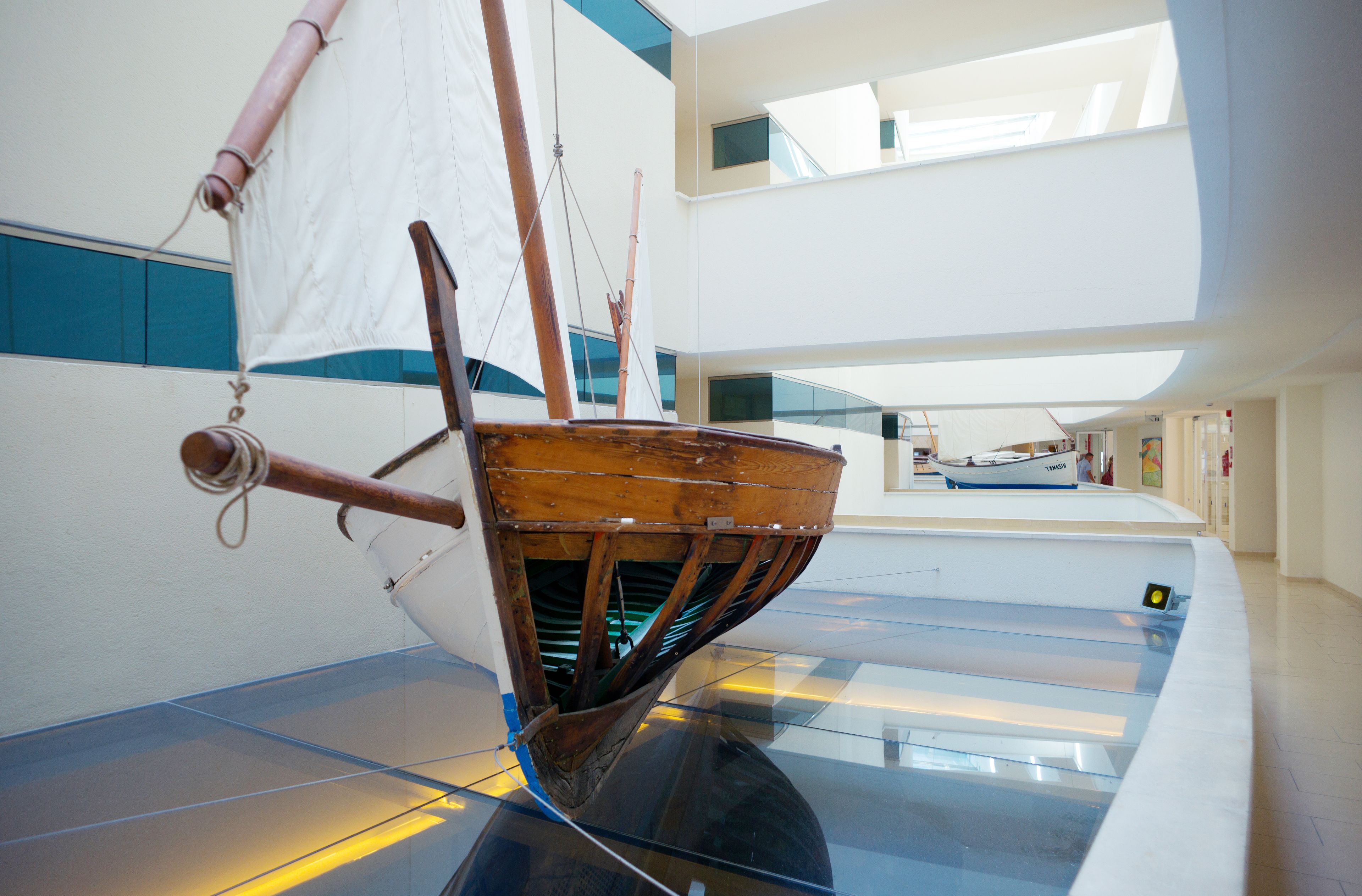Een model van een schip in een overdekte ruimte, met een glazen vloer, moderne architectuur en uitzicht op de lucht.