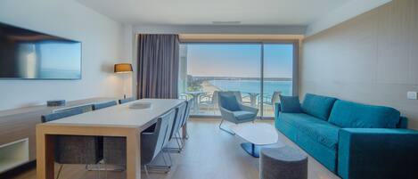 Ein modernes Hotelzimmer mit Essbereich, einer Couch und einem großen Fenster mit Meerblick.