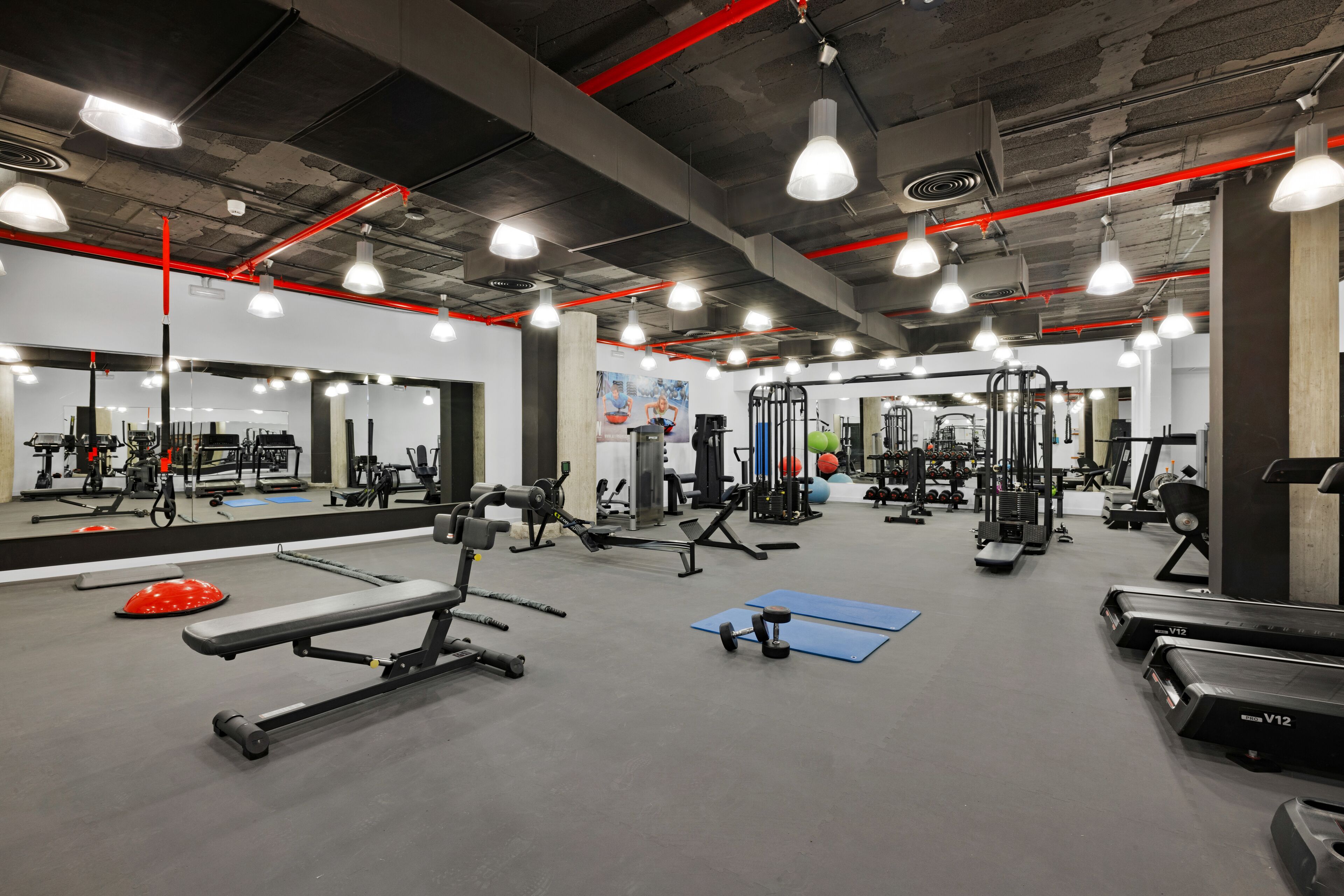 Une salle de sport équipée de divers appareils d’exercice, de miroirs et dotée d’un éclairage d’ambiance rouge.