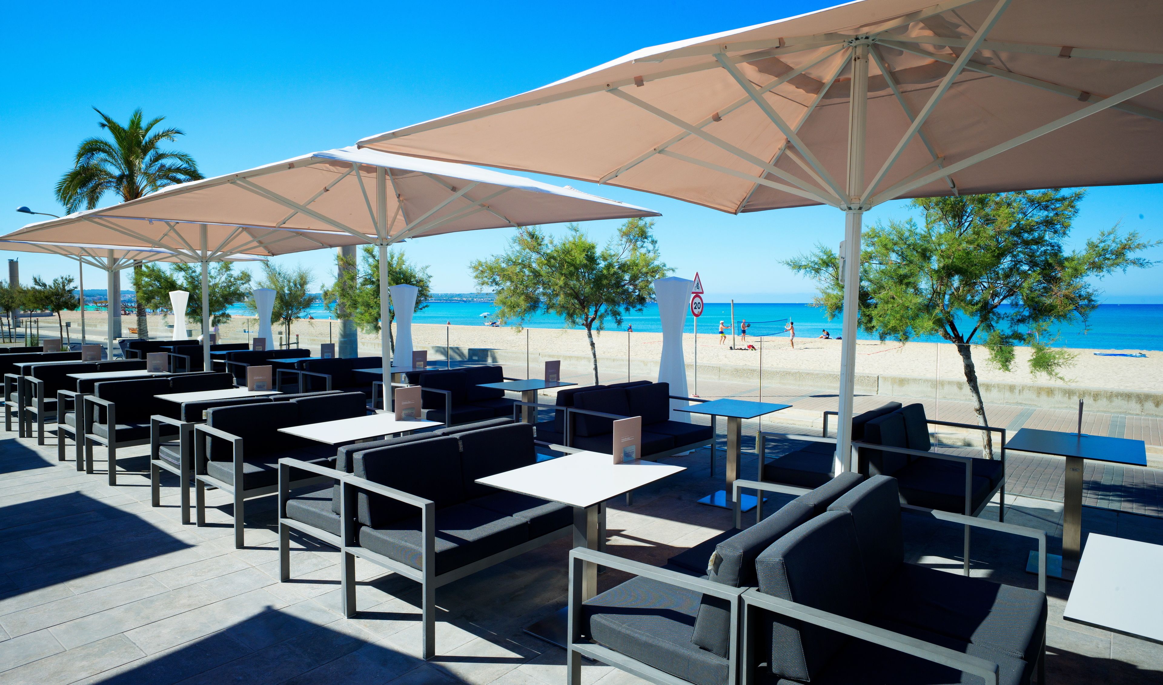 Espace extérieur aménagé avec des tables et des chaises, des parasols et une vue sur la plage et l’océan.