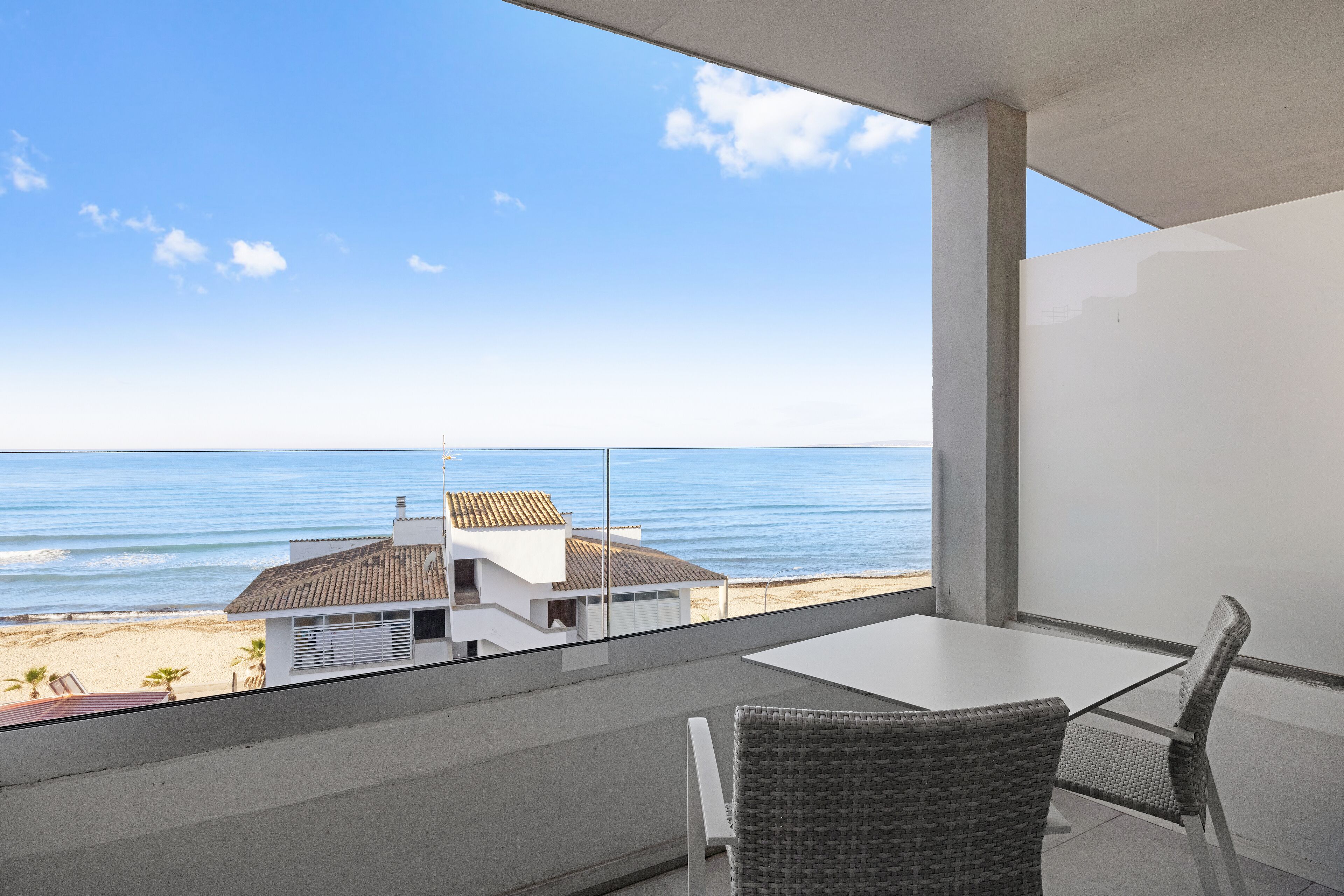 A balcony with a view of the sea, a white table, and wicker chairs.