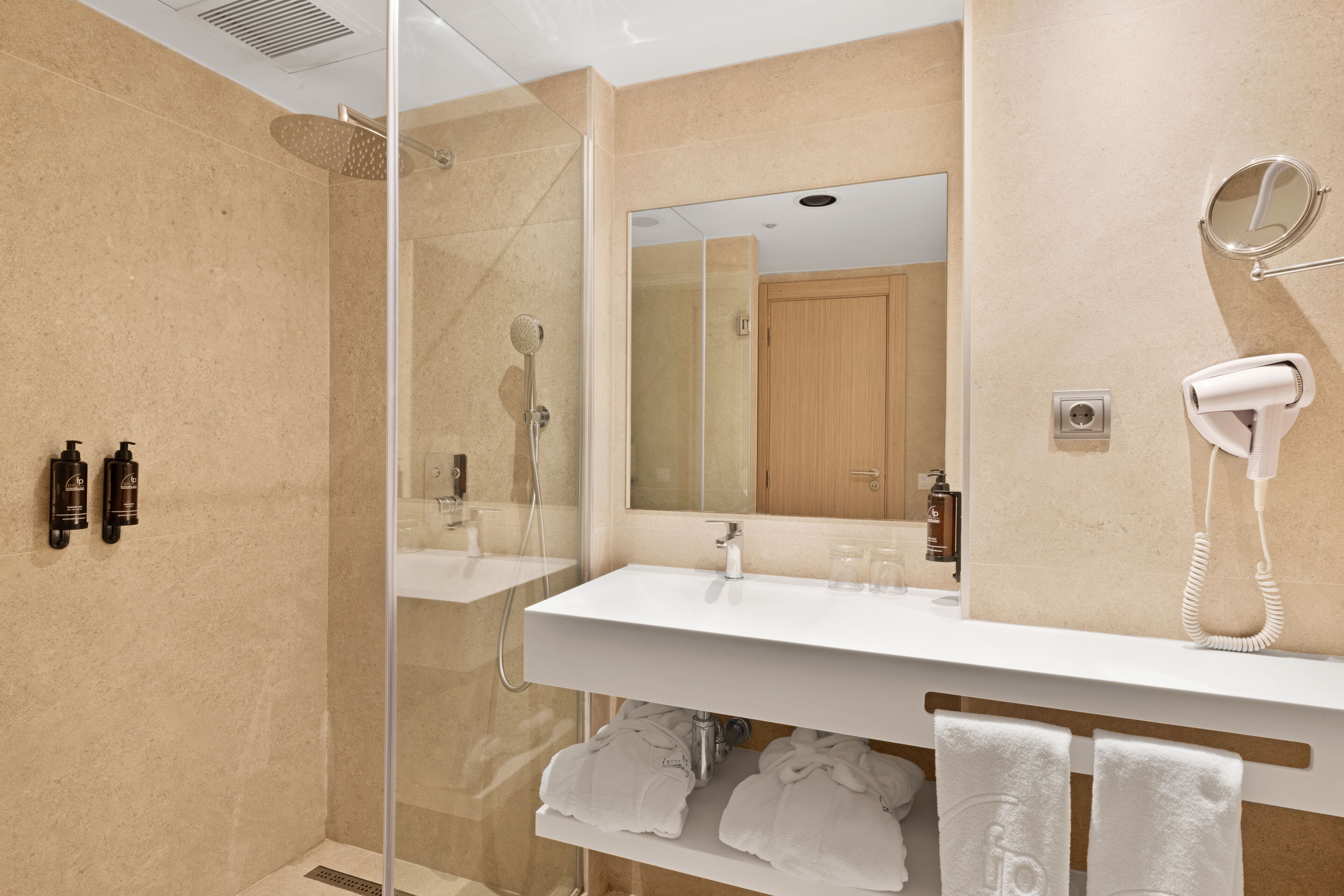 A modern bathroom with a glass-enclosed shower, a white sink, a mirror, and a hairdryer.