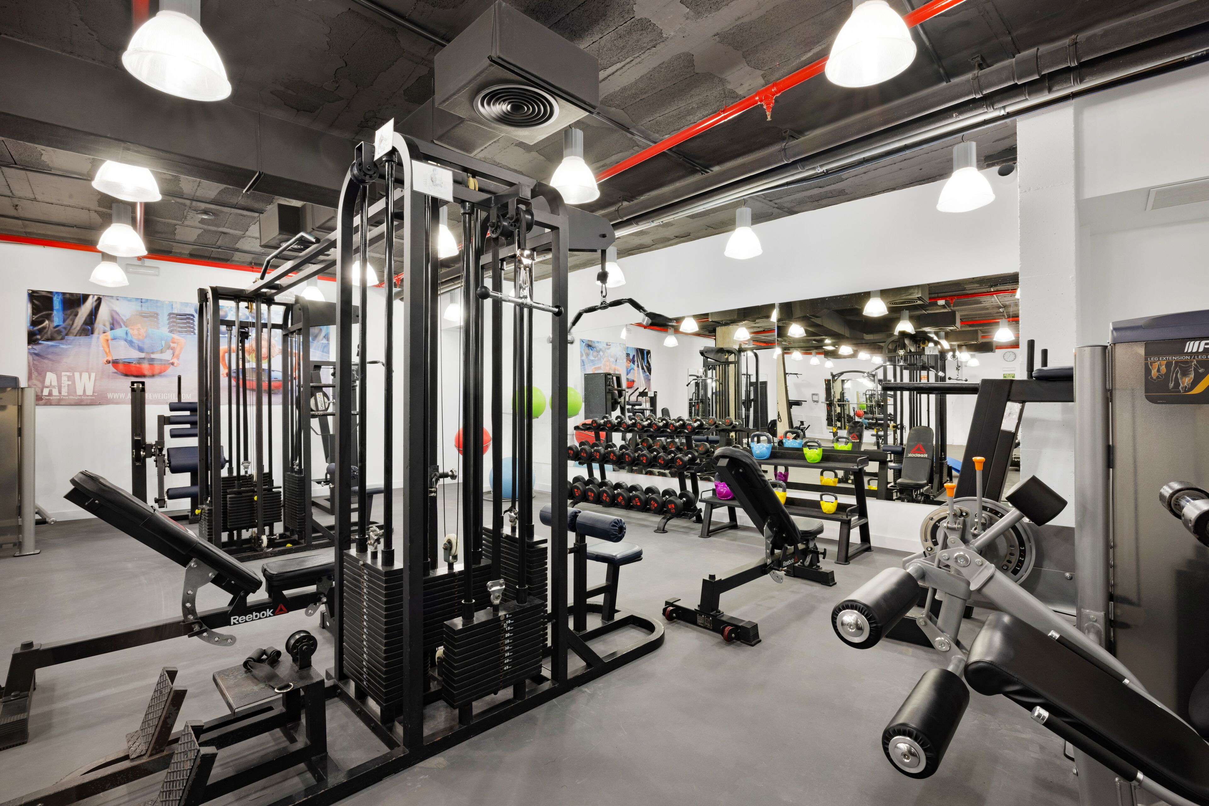 Een sportschool met diverse fitnessapparaten, waaronder krachtapparaten en gewichten.