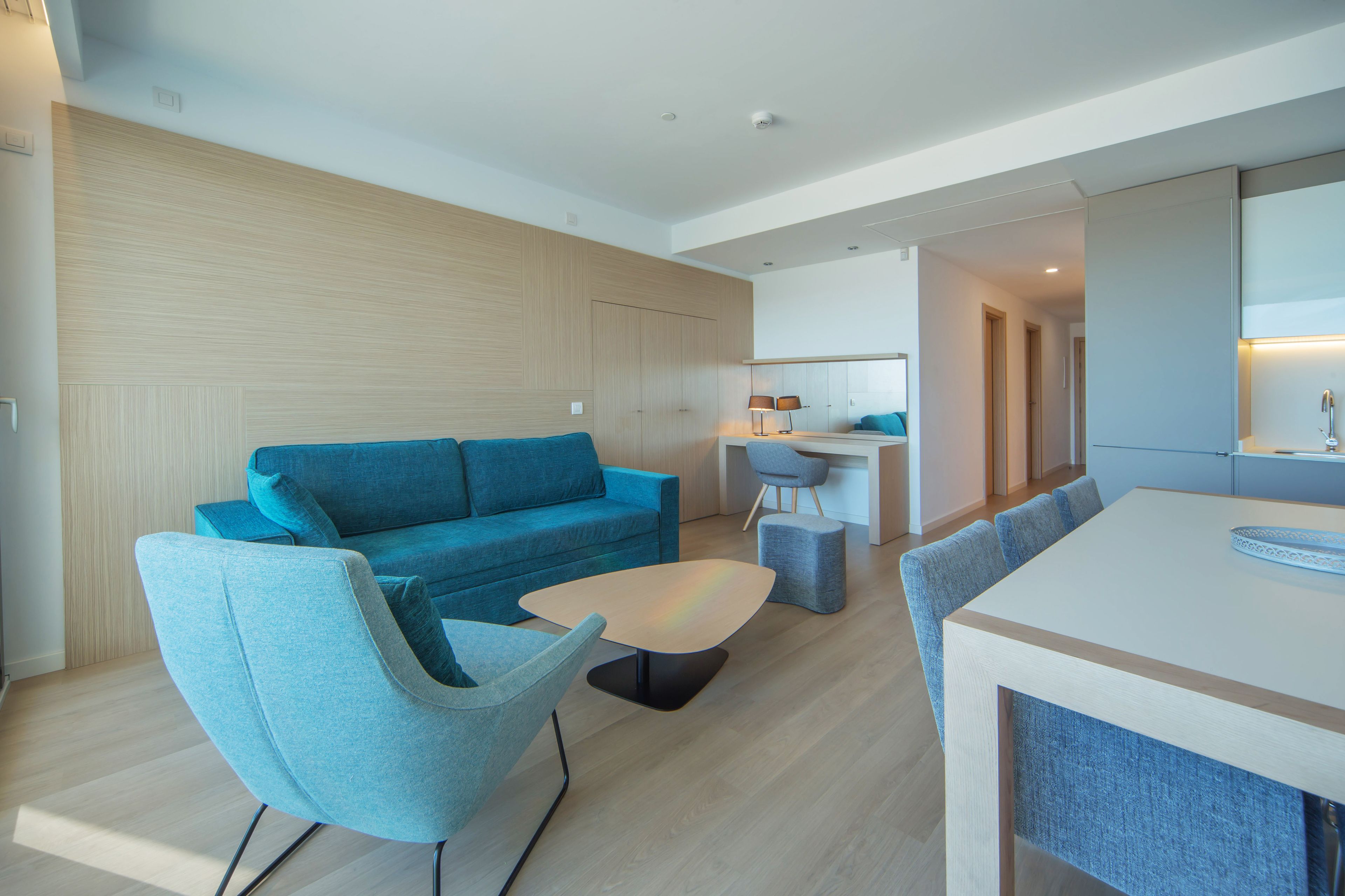 Una sala moderna con un sofá azul, una mesa de centro y un comedor con sillas.