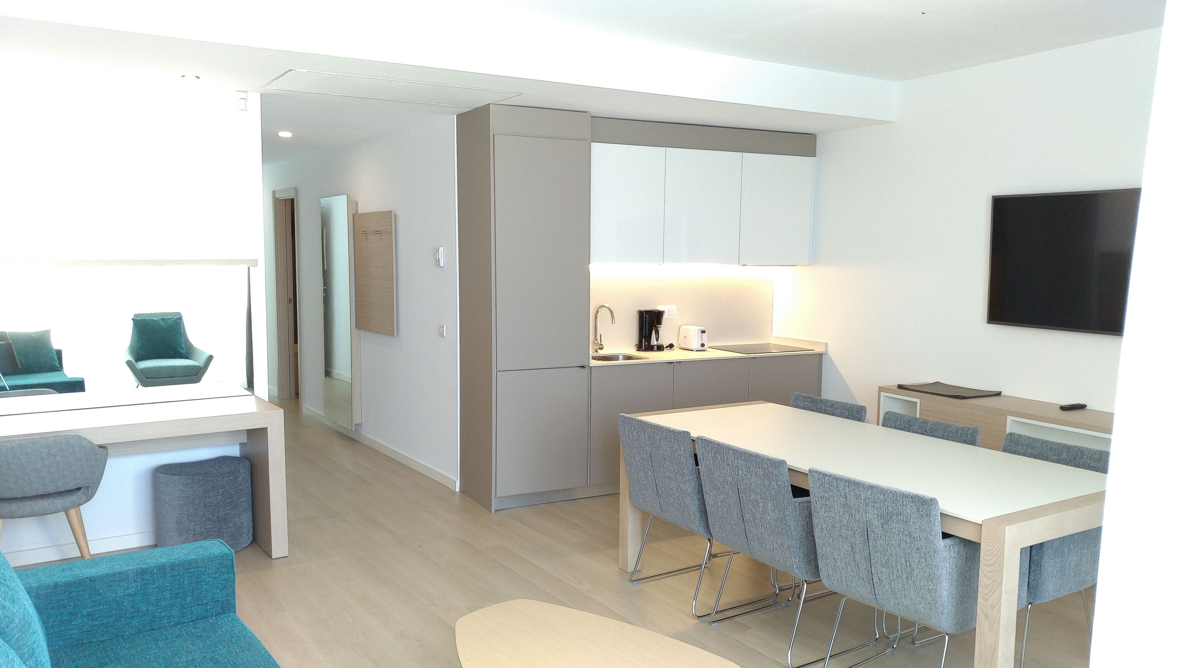 A modern kitchen with a dining area, a TV mounted on the wall, and a view of the adjacent living room.