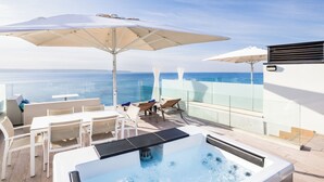 Une terrasse sur le toit dotée d’un jacuzzi, de chaises longues et de parasols, offrant une vue sur l’océan.