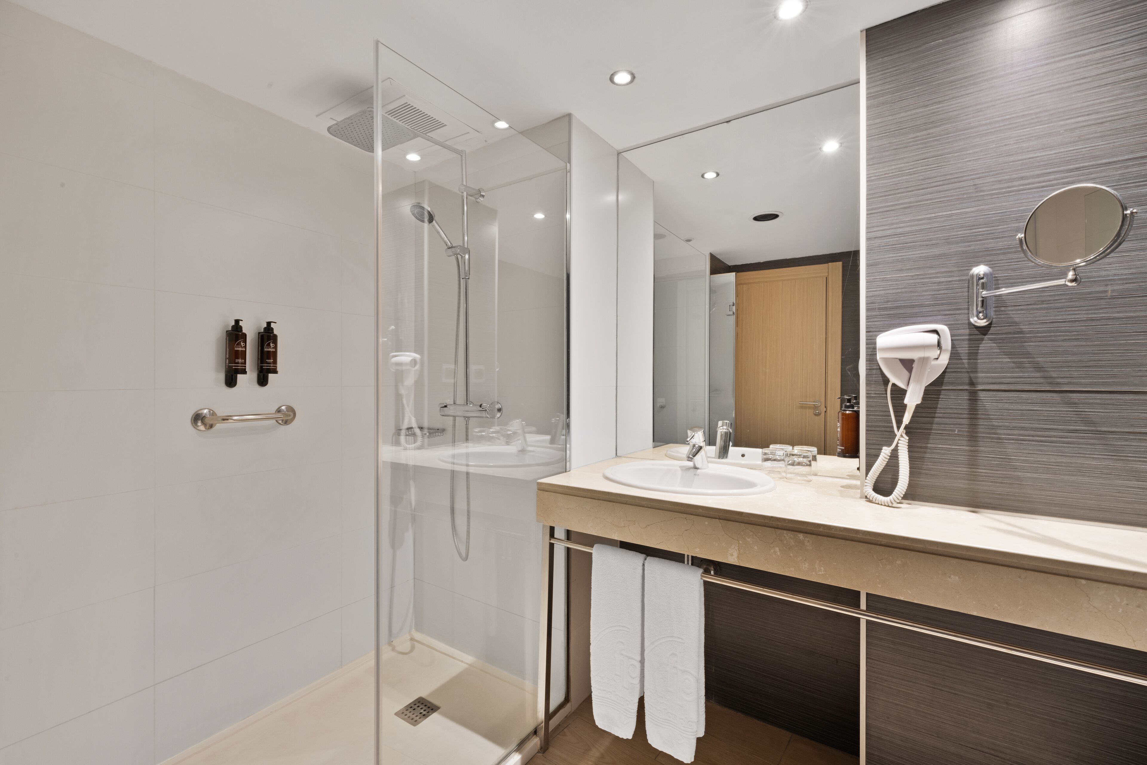 A modern bathroom with a glass-enclosed shower, a large mirror, and a vanity with a sink and towel rack.