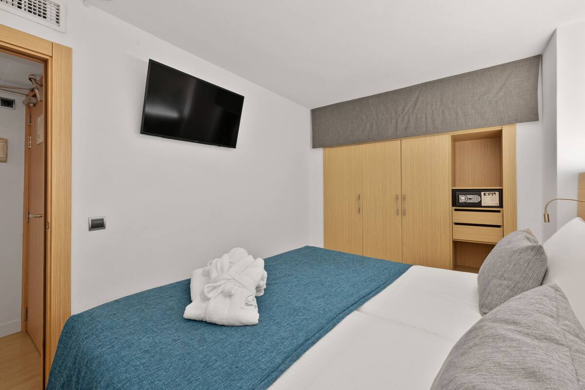 Un dormitorio con una cama, un televisor montado en la pared y un armario.