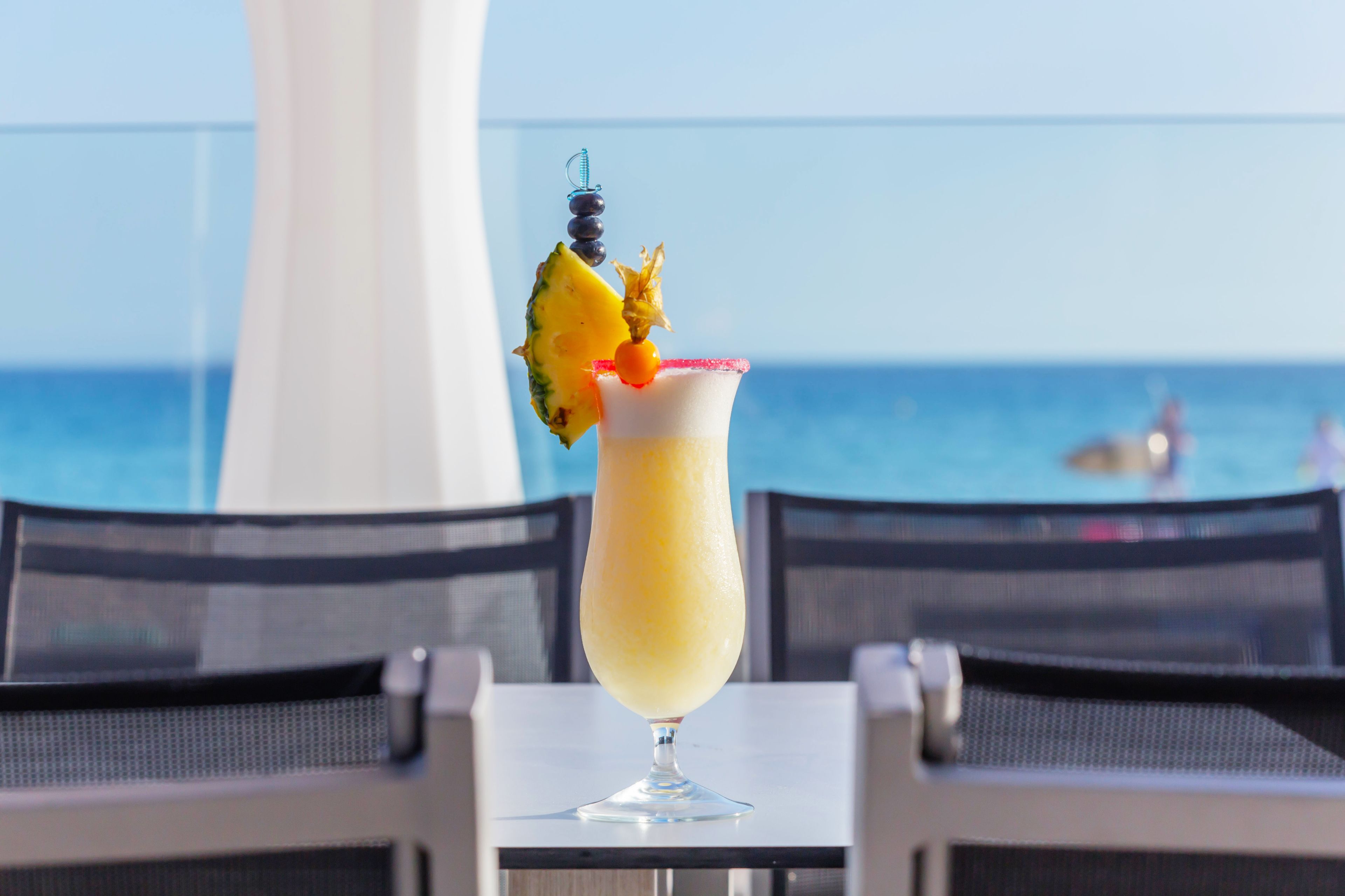 Ein Cocktailglas mit tropischer Dekoration auf einem Tisch am Meer.