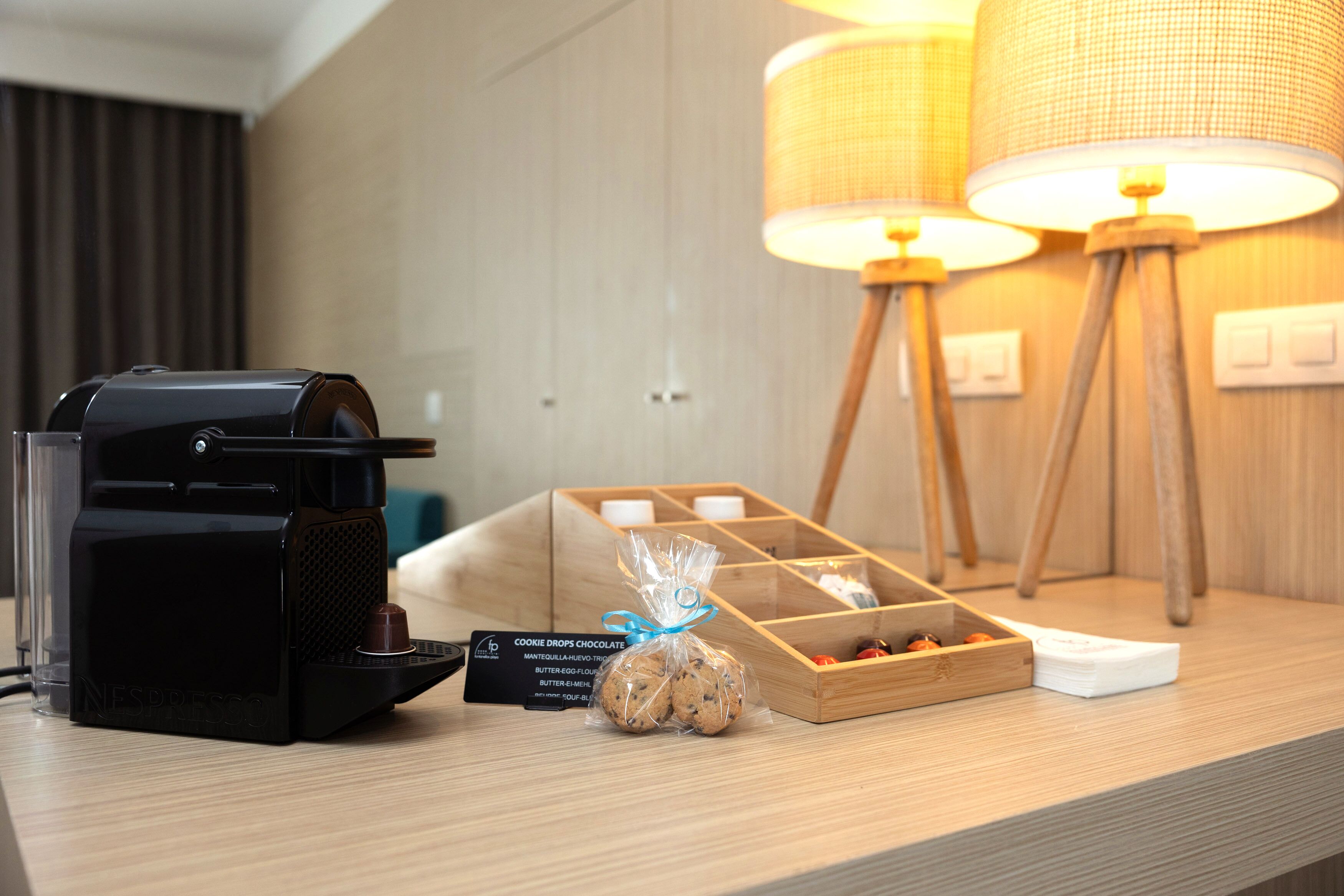A coffee machine, a tray with cookies, and a lamp on a wooden table.