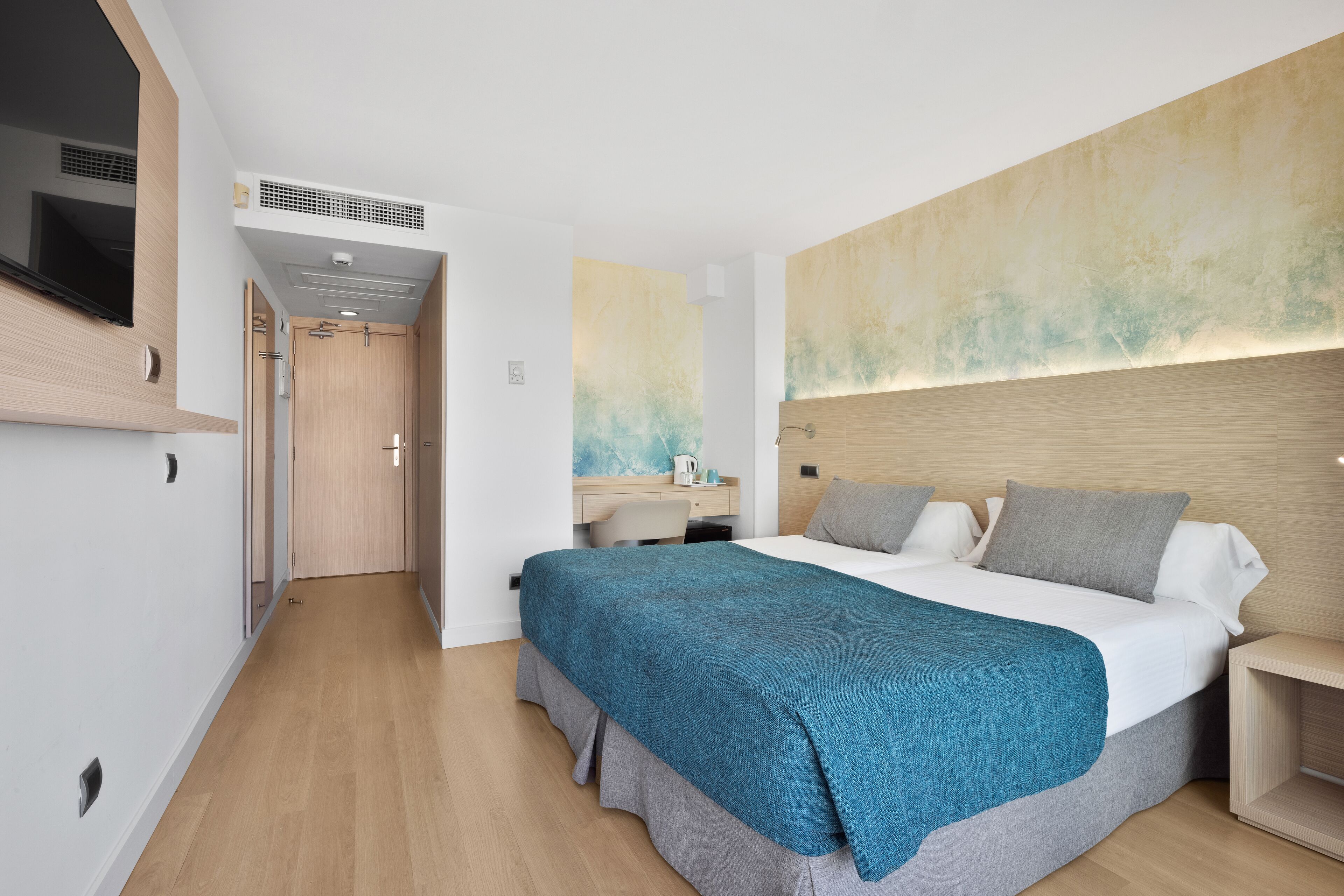A modern hotel room with a large bed, a desk, and a wardrobe.