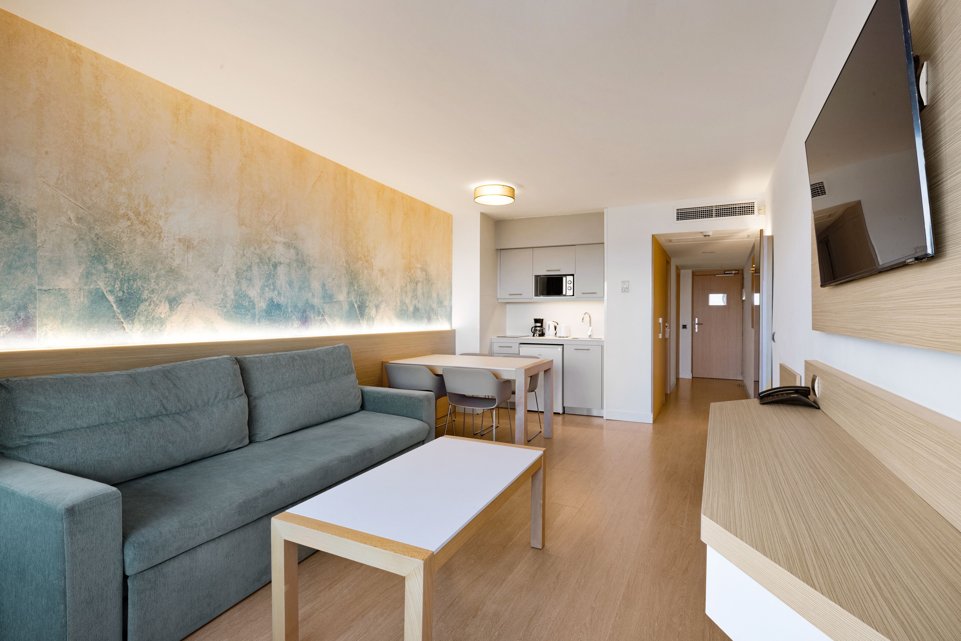 Un salon moderne avec un canapé gris, une table basse blanche et un coin cuisine à l’arrière-plan.