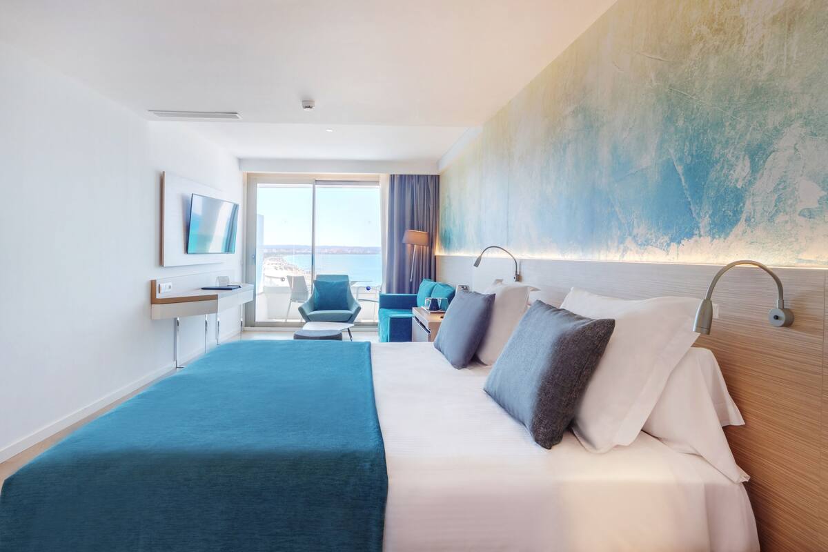 Habitación de hotel con una cama grande, un escritorio con silla, televisión y vista al mar.