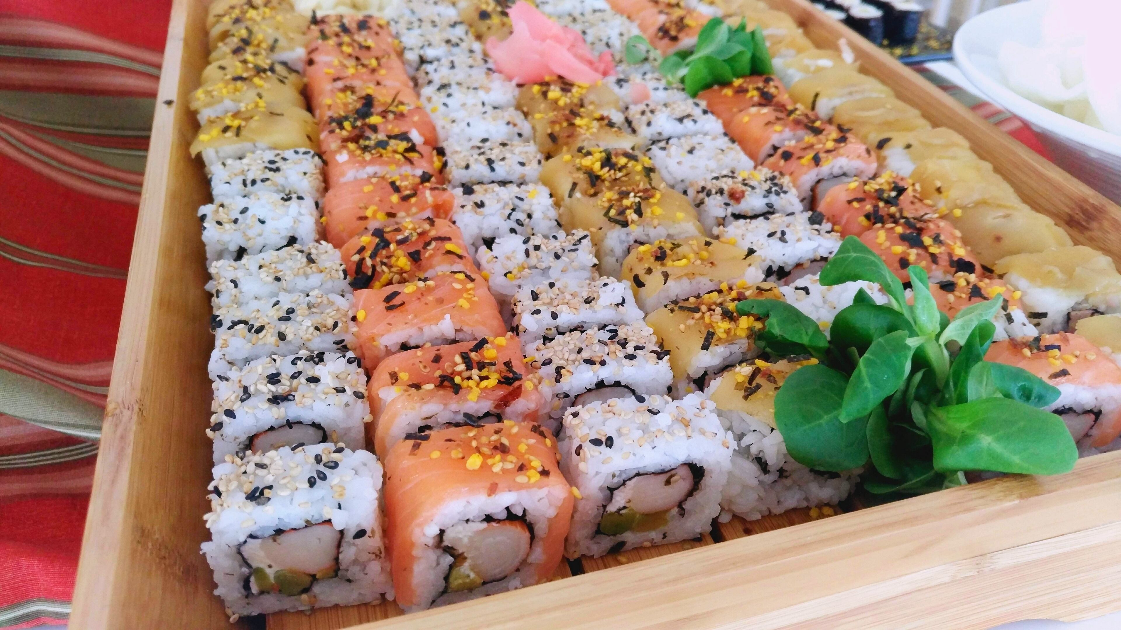 A wooden tray with various sushi rolls, including salmon and tuna, garnished with sesame seeds and wasabi.