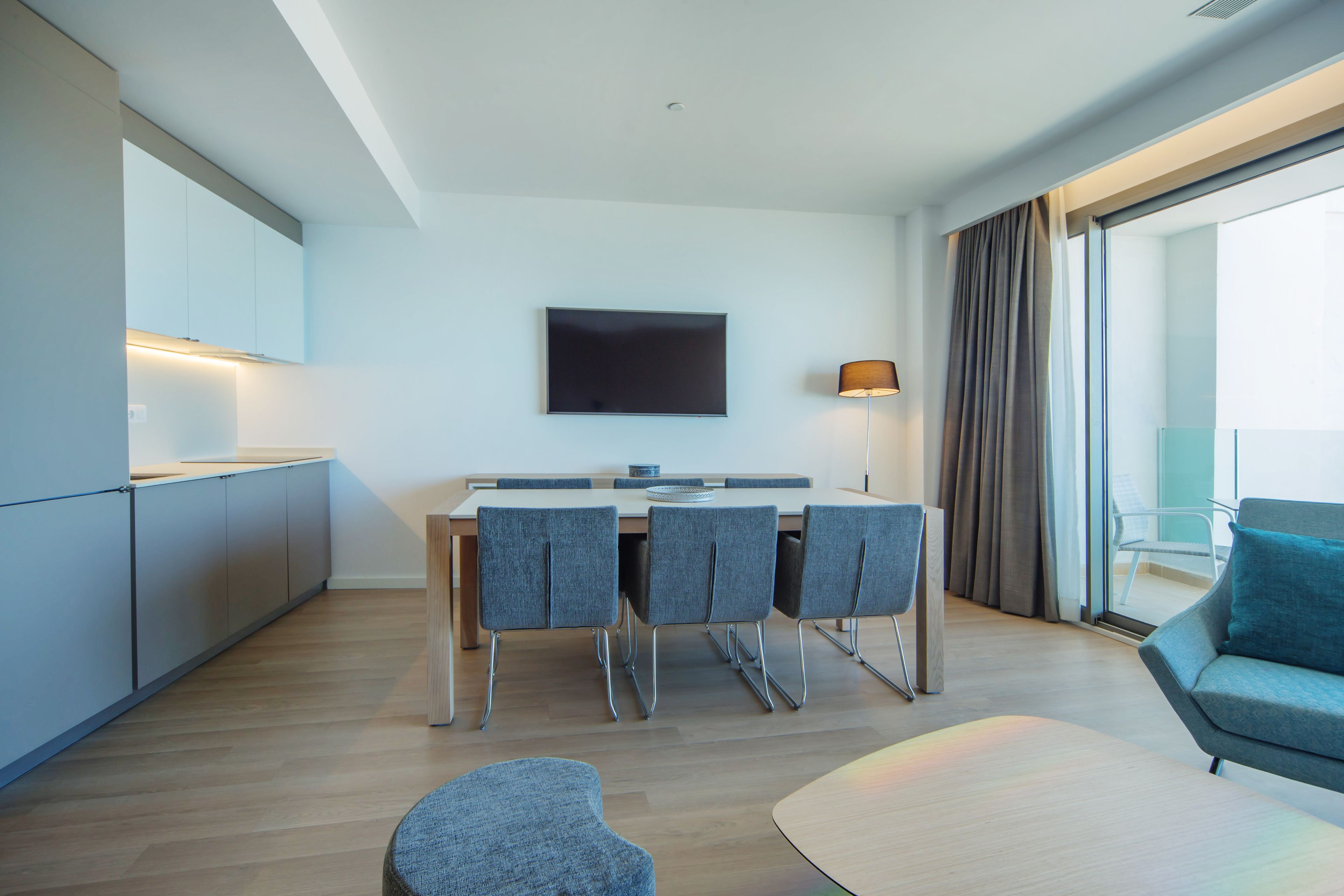 A modern kitchen with a dining area, a flat-screen TV, and a seating area with a sofa and armchair.