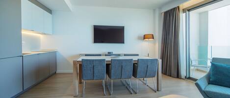 A modern kitchen with a dining area, a flat-screen TV, and a seating area with a sofa and armchair.