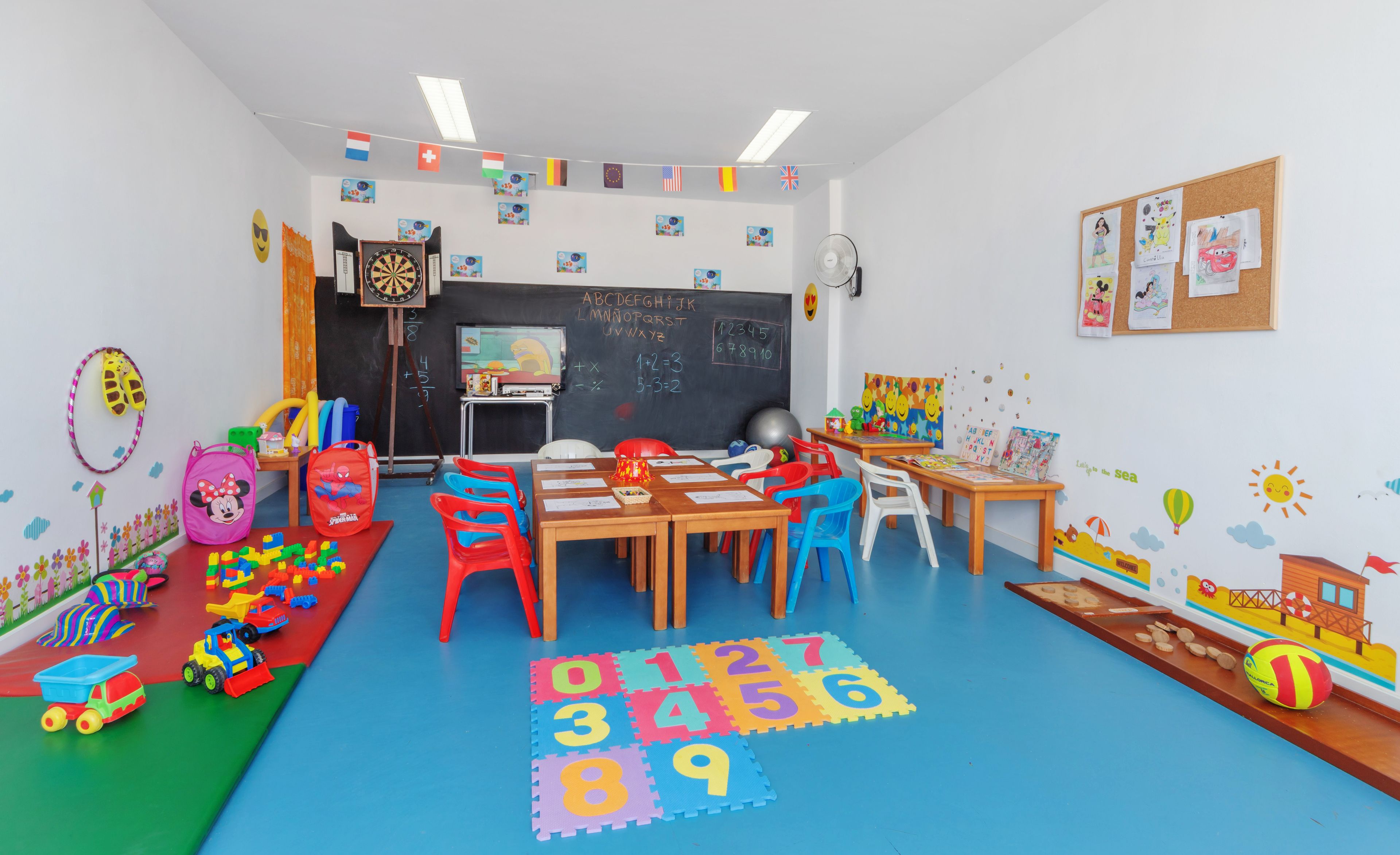 A classroom with educational toys, a blackboard, and a bulletin board with children's drawings.