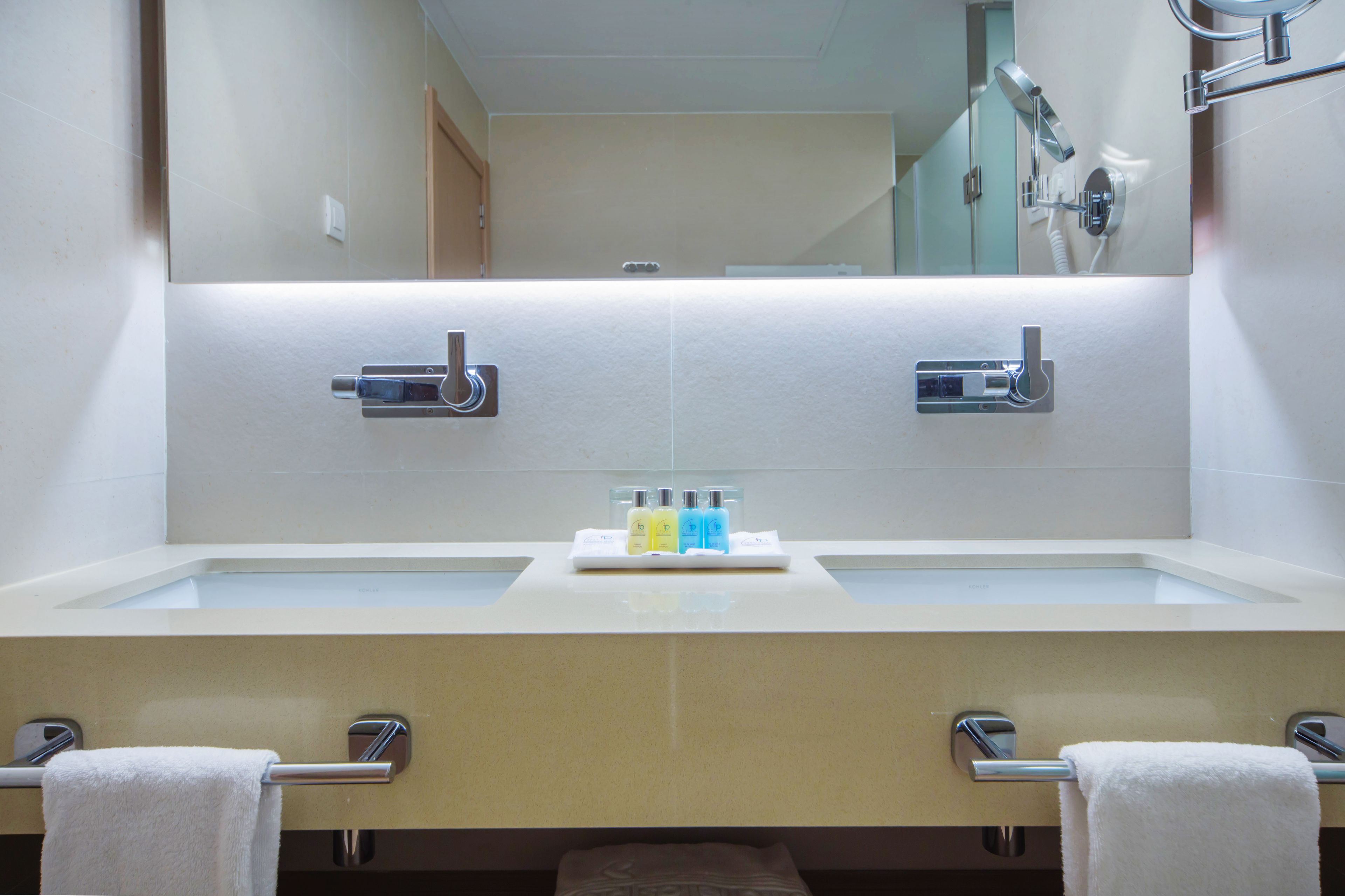 A modern bathroom with a large mirror, two sinks, and a towel rack.