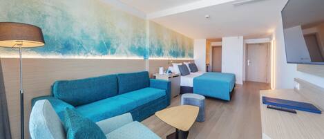 A modern hotel room with a blue sofa, a small table, a bed, and a TV.