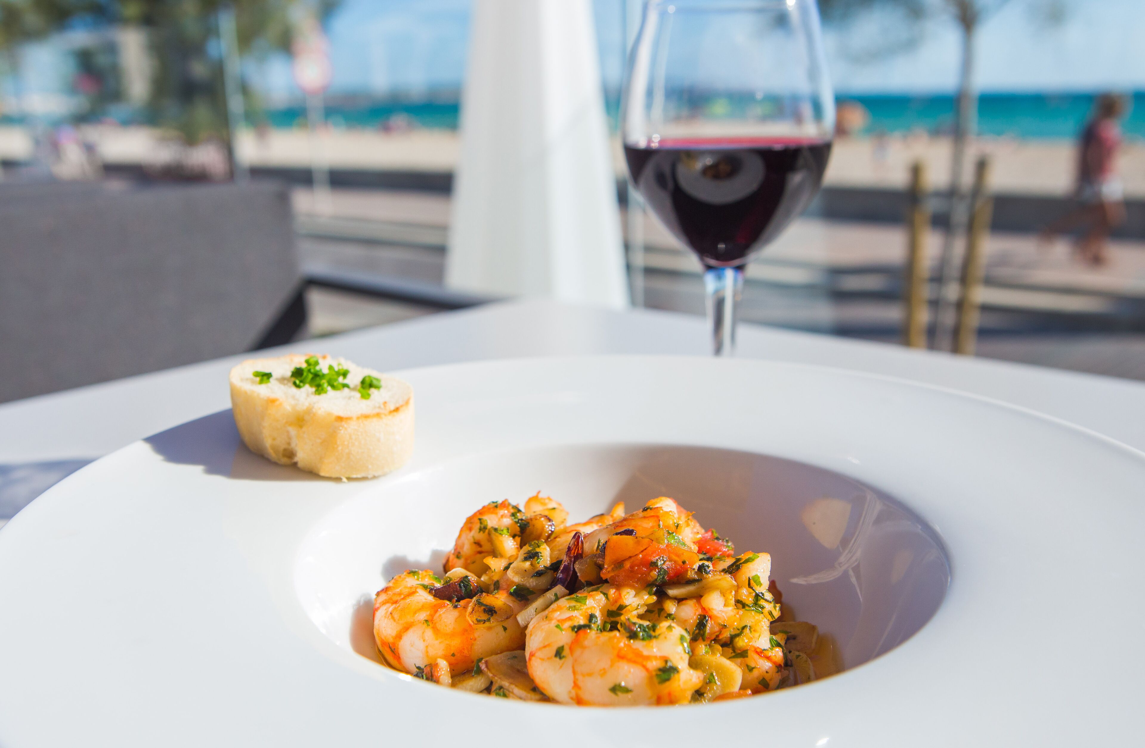 A seafood dish on a white plate with a glass of red wine in the background.