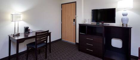 Habitación de hotel con escritorio, silla, televisor, lámpara y armario.