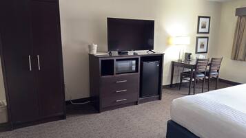 Habitación de hotel con cama, escritorio con televisor, microondas, refrigerador pequeño, una silla y armario.