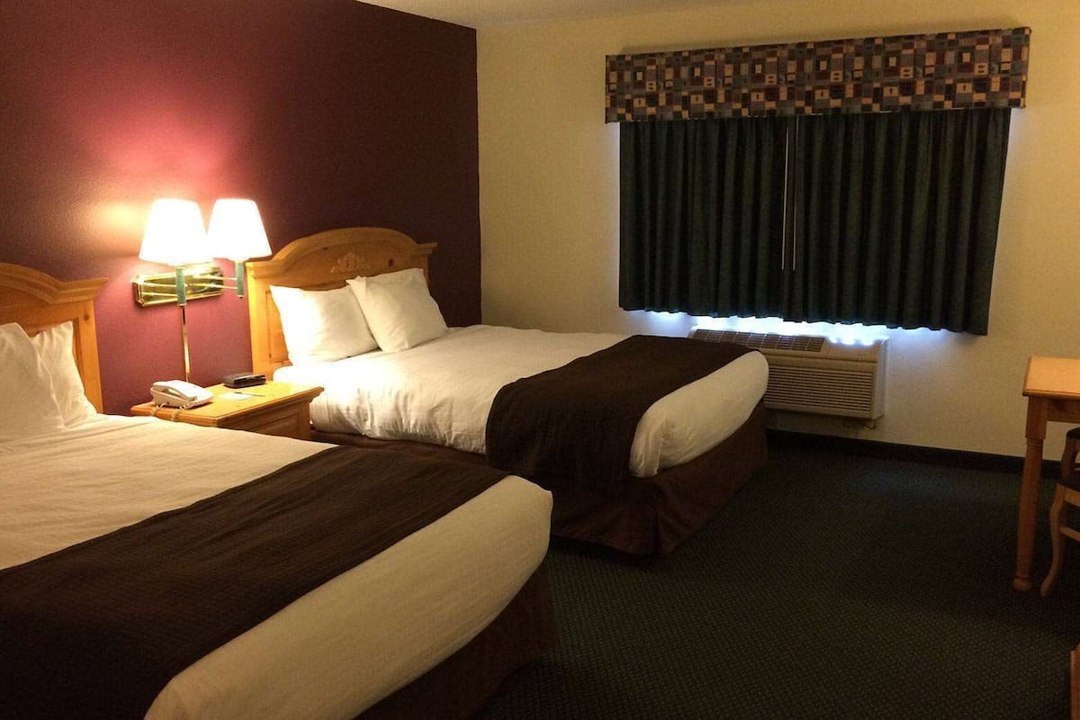 Ein Hotelzimmer mit zwei Betten, einem Schreibtisch, einem Stuhl, einer Lampe und einem Fenster mit Vorhängen.