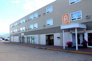 A multi-story hotel with a modern design, featuring a prominent 'ACORN' sign, a covered entrance, and a parking lot in the foreground.